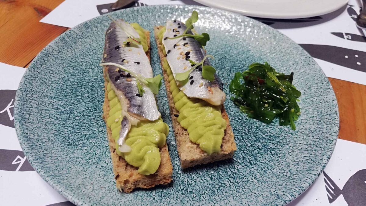 Tosta de pan de cereales, hummus de aguacate y lomo de sardina al vinagre.