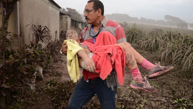 Un hombre ayuda a una niña afectada en El Rodeo, Escuintla (Guatemala) tras la erupción del volcán de Fuego, que ha dejado al menos 25 muertos, 20 heridos y más de 1,7 millones de personas afectadas